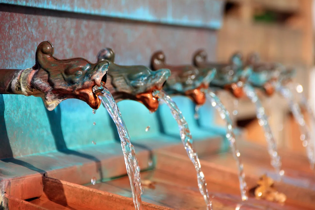 A cast-iron nasone street fountain running water in Rome, with a baroque fountain out of focus behind