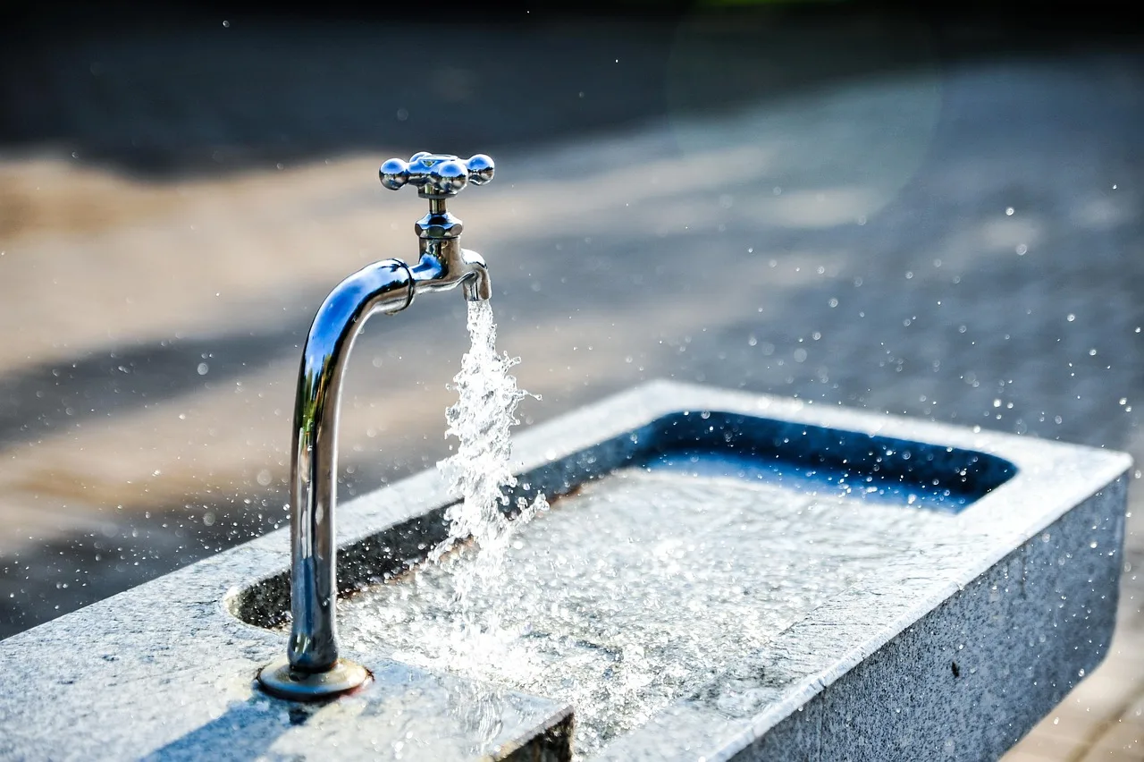 A kitchen tap crusted with limescale running water into a glass