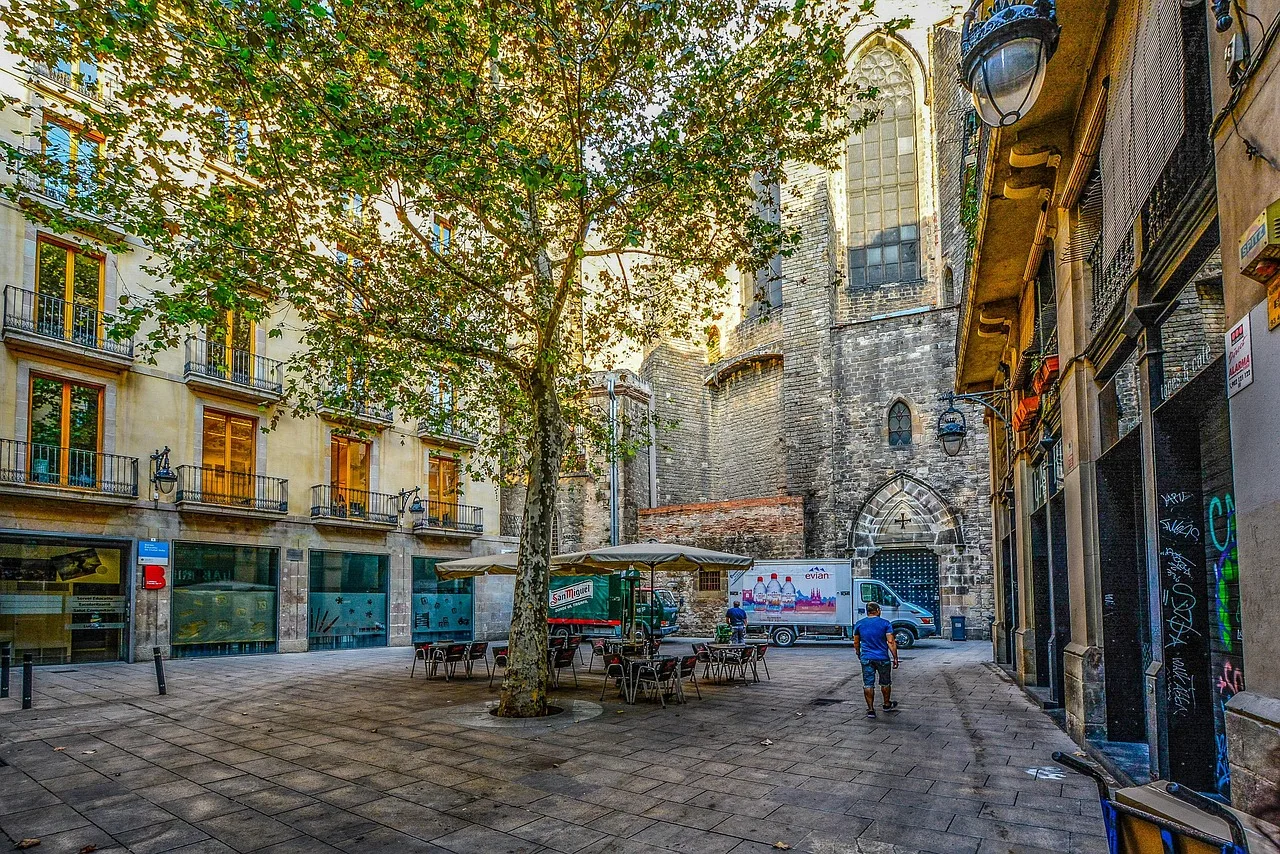 A narrow stone street in Barcelona's Gothic Quarter at dawn, a resident passing half-raised shop shutters
