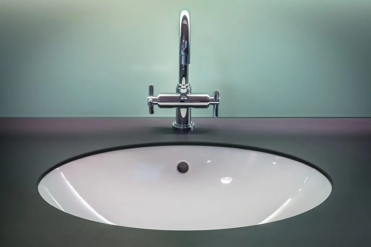 A white basin with two separate pillar taps, one hot and one cold, and a plug in the drain
