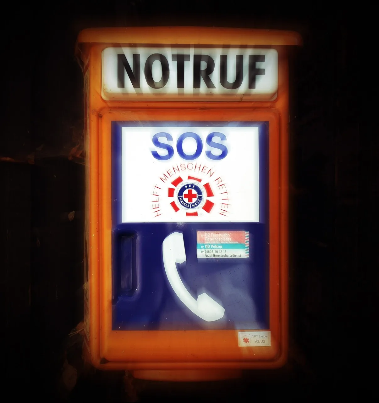 A hand holding a phone showing an emergency dial pad against a blurred street at dusk