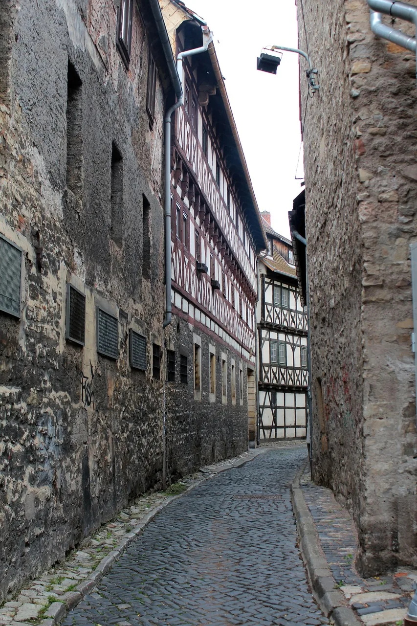 A narrow stone lane between wooden machiya buildings at dusk, with a small sign on a wall