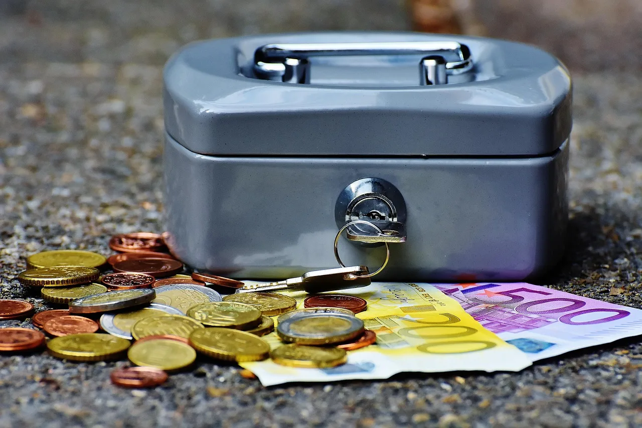 An open cash box of coins and notes next to a printed QR code on a market stall table