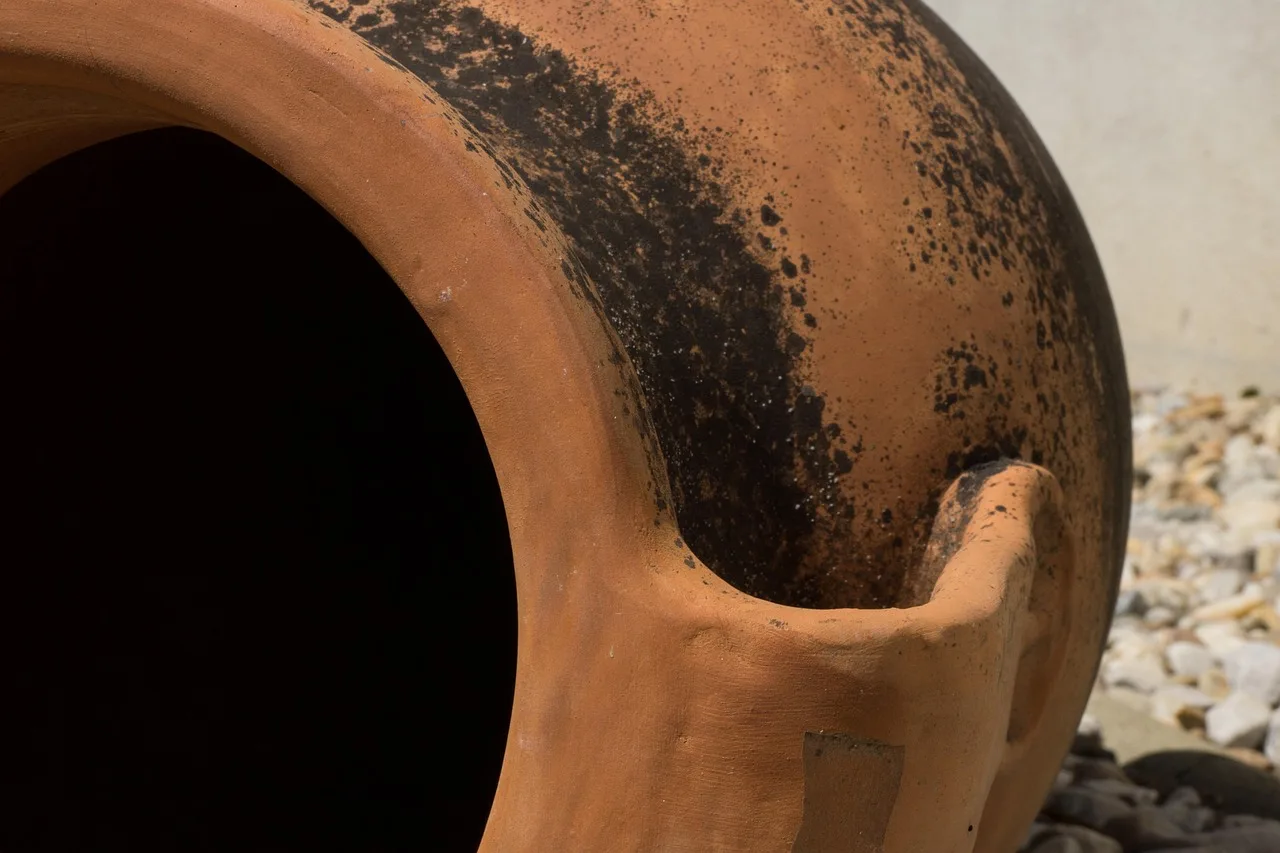 Wine being poured from a clay jug into an already full glass at a laid table