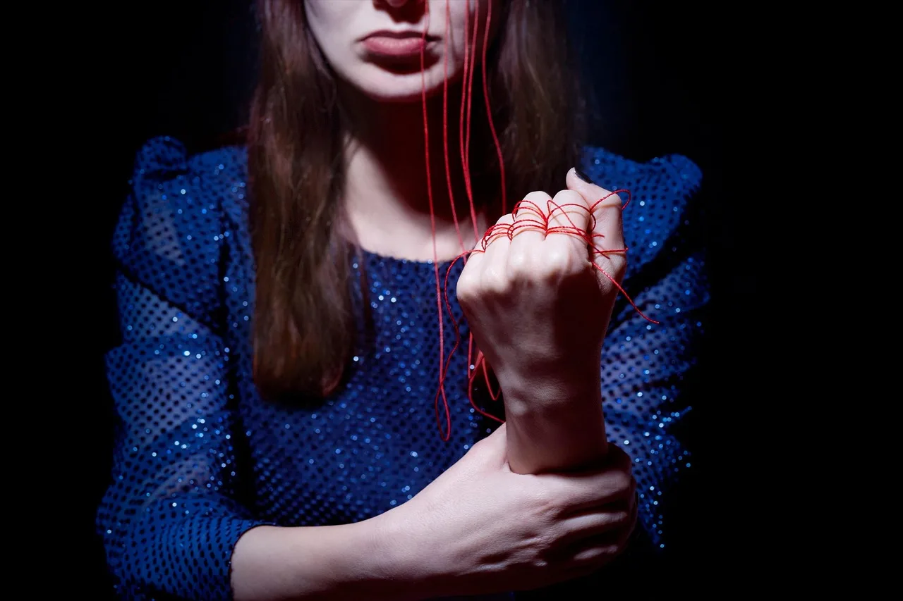 Two hands tying a coloured string bracelet onto another person's wrist