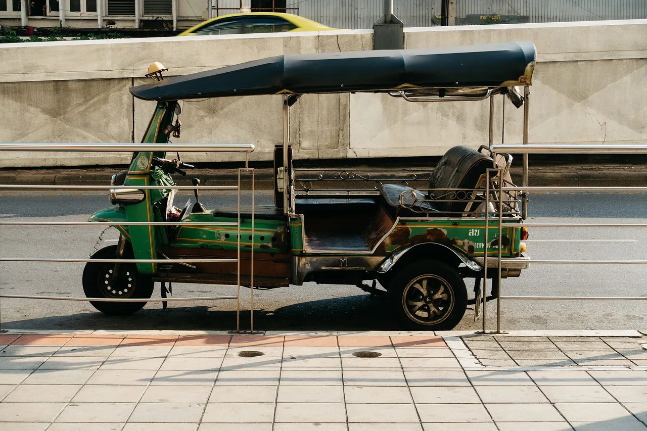 A tuk-tuk waiting at the kerb beside a temple wall in Bangkok