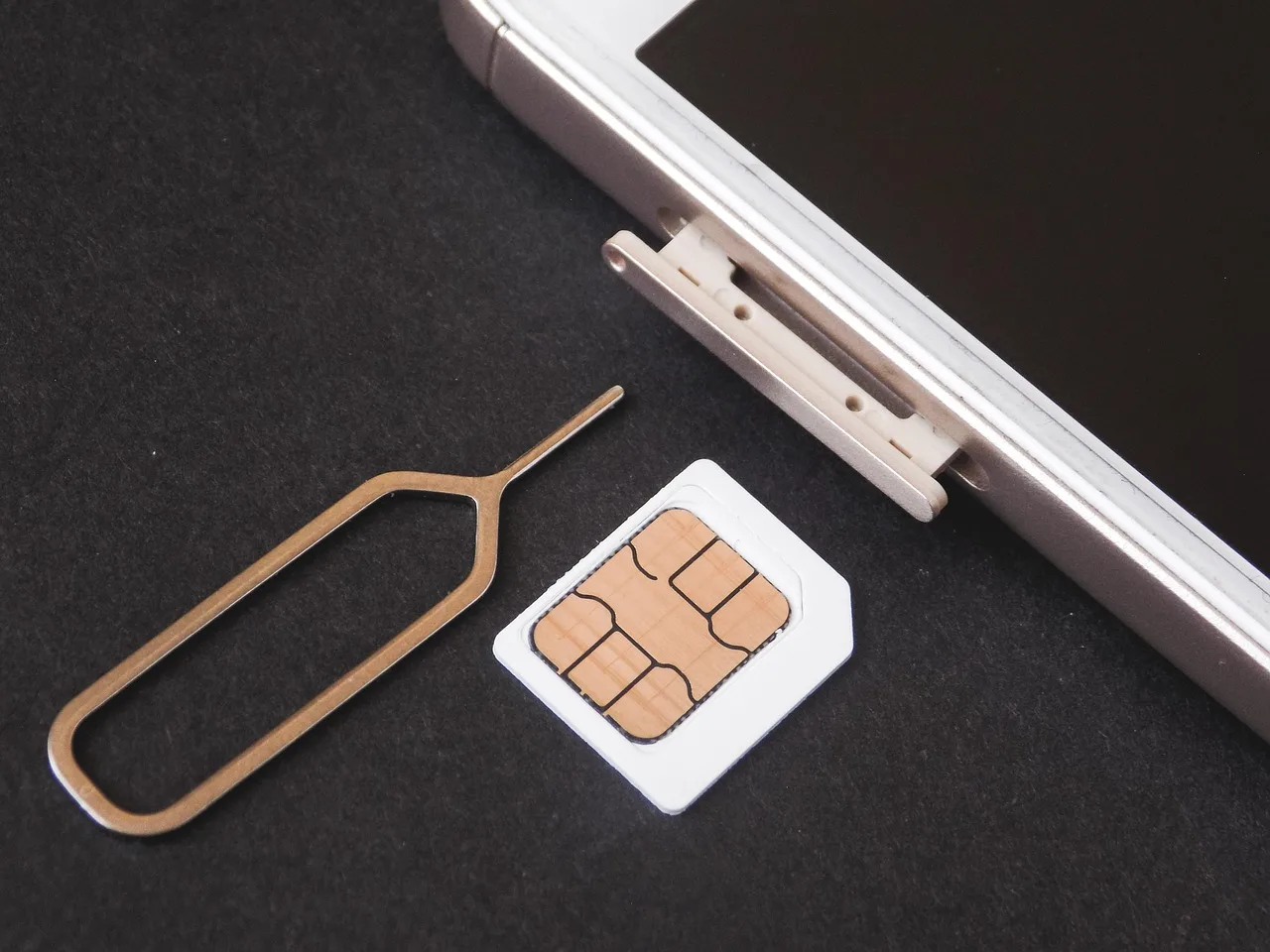 A SIM tray ejected with a paperclip, the small card lying beside it on a table