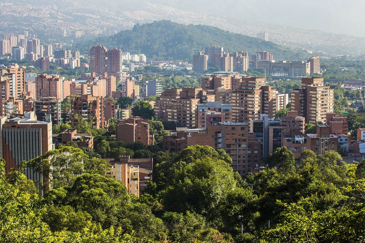 A curving tree-lined residential street in Medellin with low-rise apartment blocks and a delivery rider at the kerb