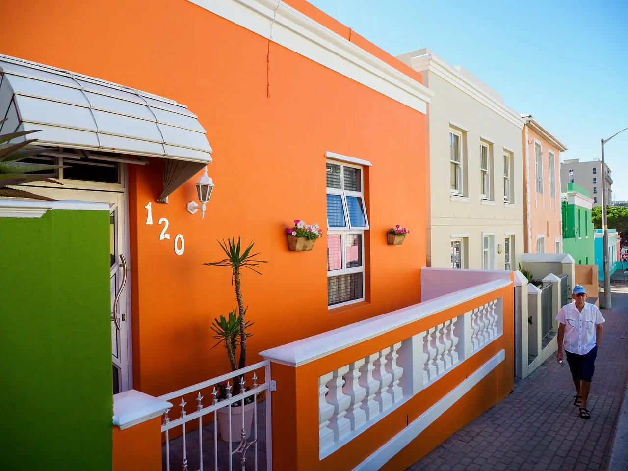 A row of flat-roofed Bo-Kaap terrace houses in different colours on a steep street, each with a raised stoep