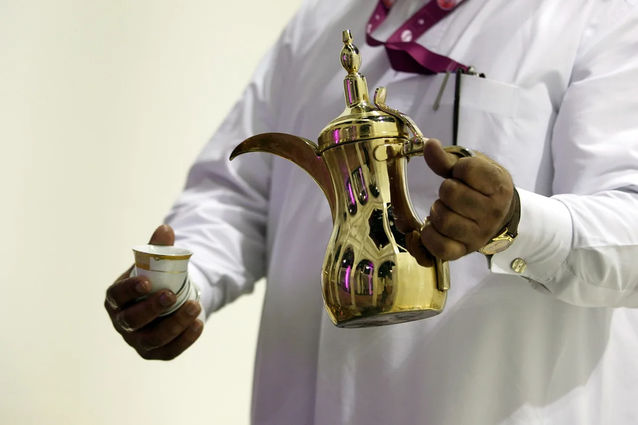 A brass coffee pot and three small handleless cups on a tray, one cup full and set apart