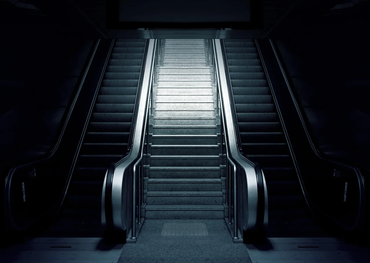 A lift at the end of a low subway passage with people and a pram waiting