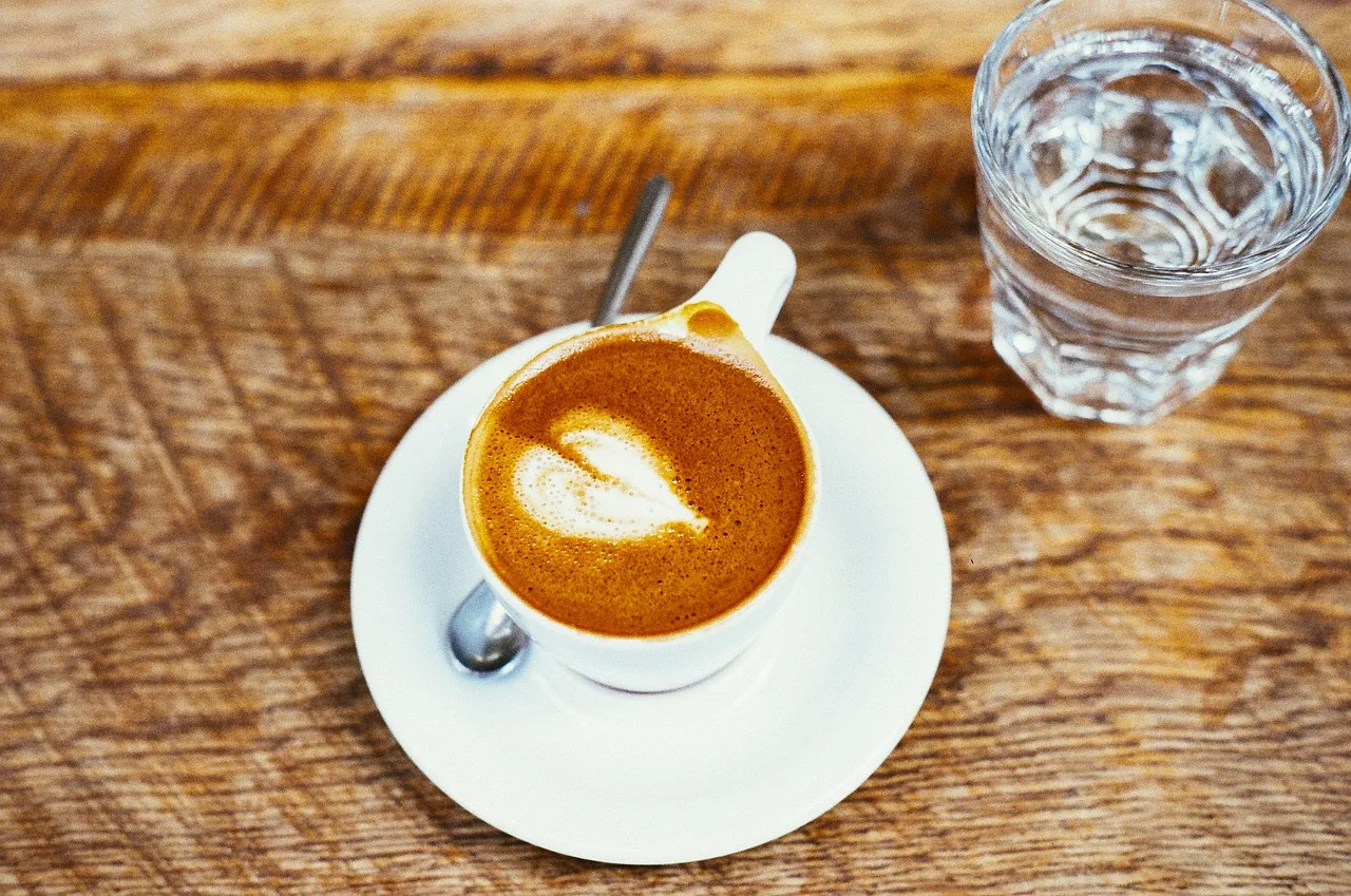 An espresso in a small white cup with a spoon and a glass of water on a bar counter