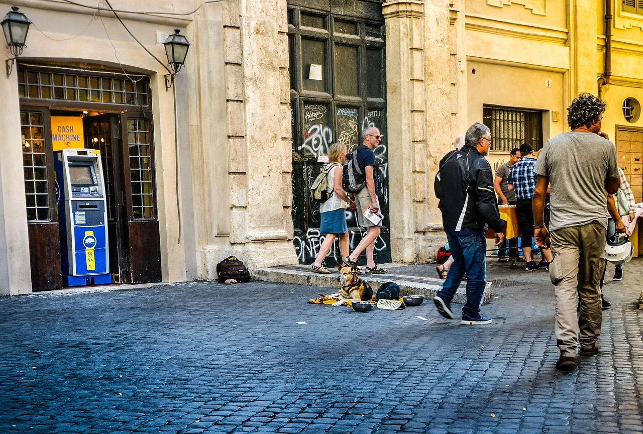 A free-standing cash machine on a busy pavement near a station, with people passing behind