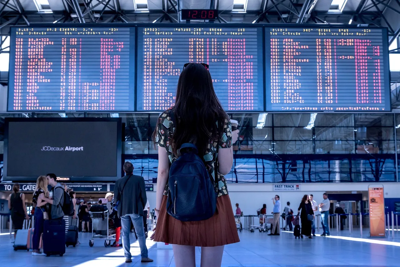 A lone passenger with a suitcase in a night-time airport arrivals hall, with border gates and exit doors ahead