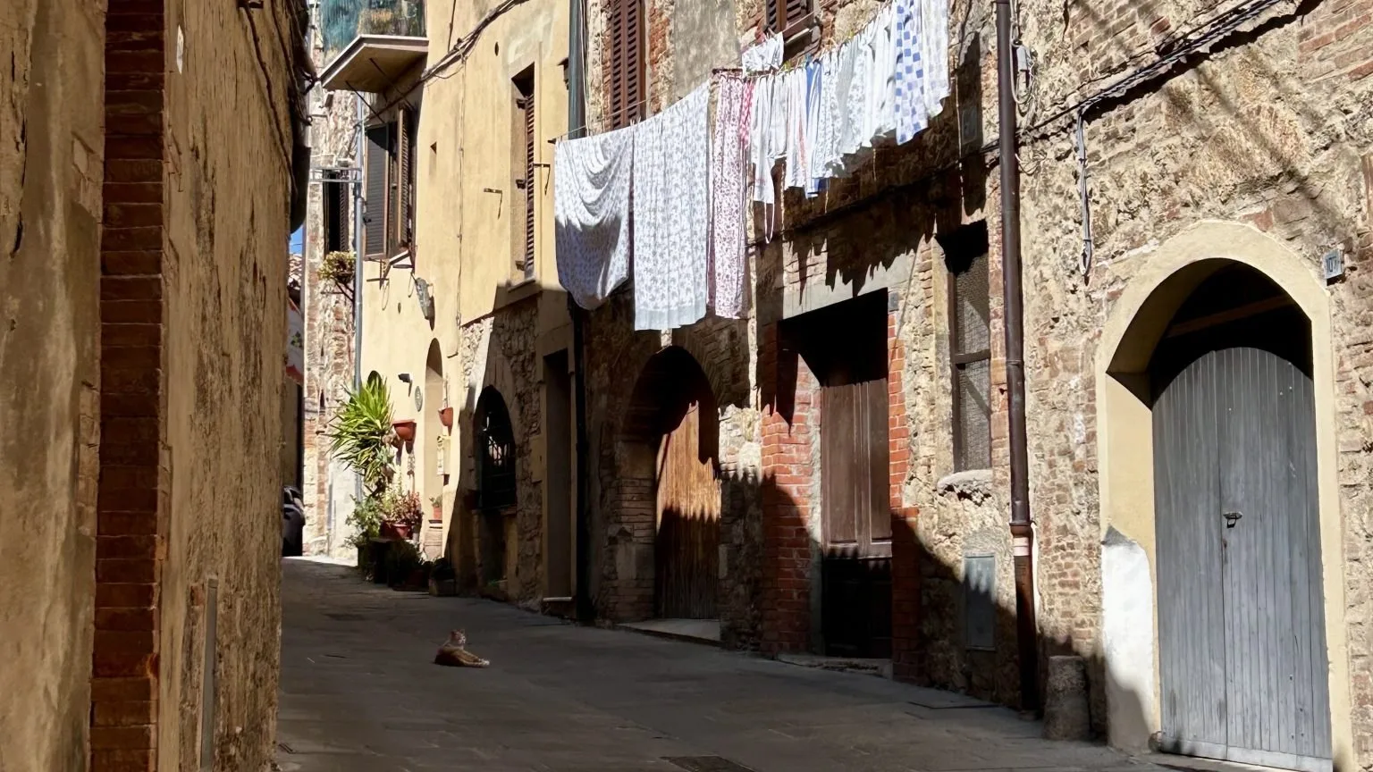 A quiet sunlit lane in a small Italian town, shutters closed against the heat.