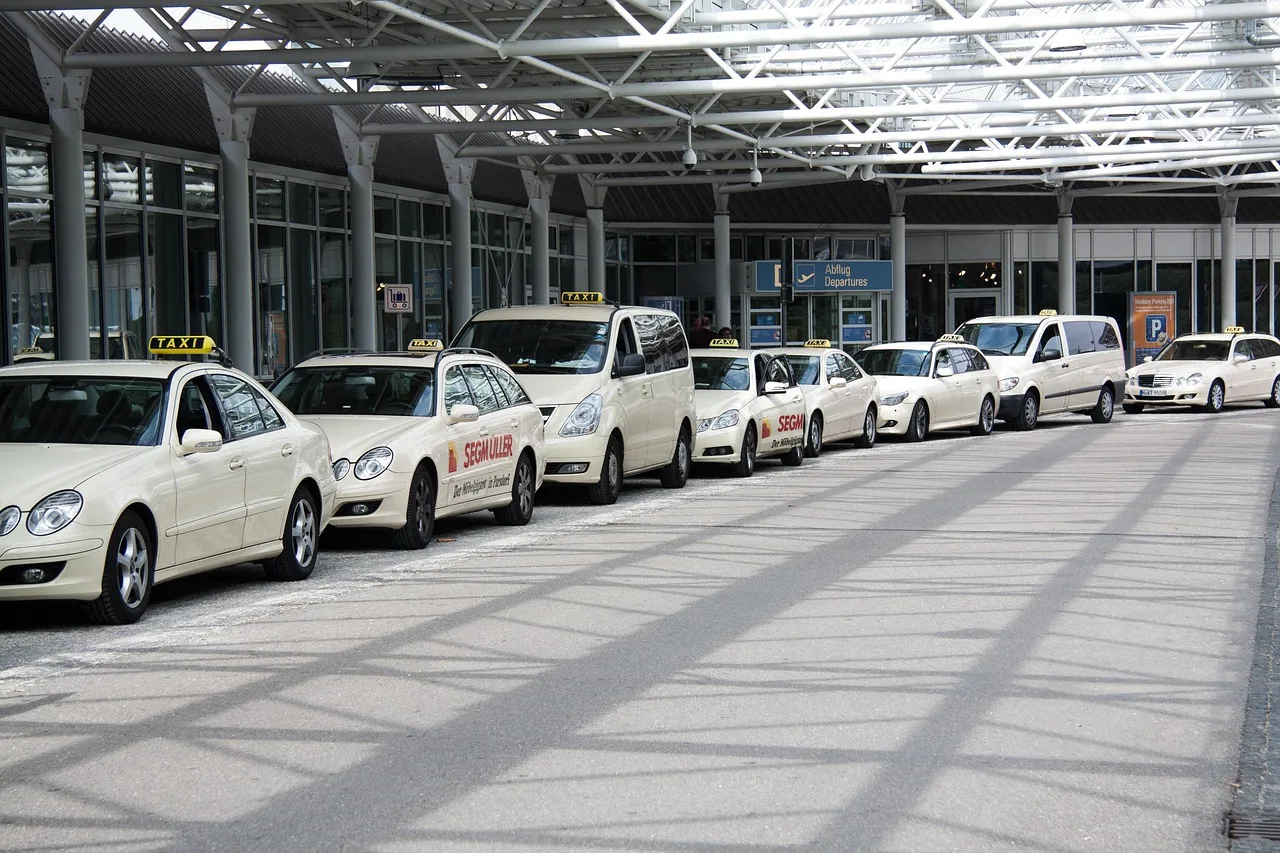 A marshalled airport taxi rank with waiting taxis and a posted fare board