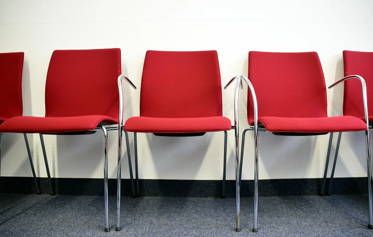 A near-empty official waiting room with fixed plastic chairs and a ticket number display