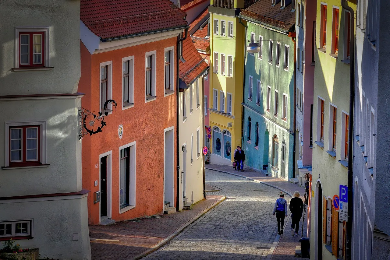 A narrow lamplit old-town street at dusk with two figures approaching ahead
