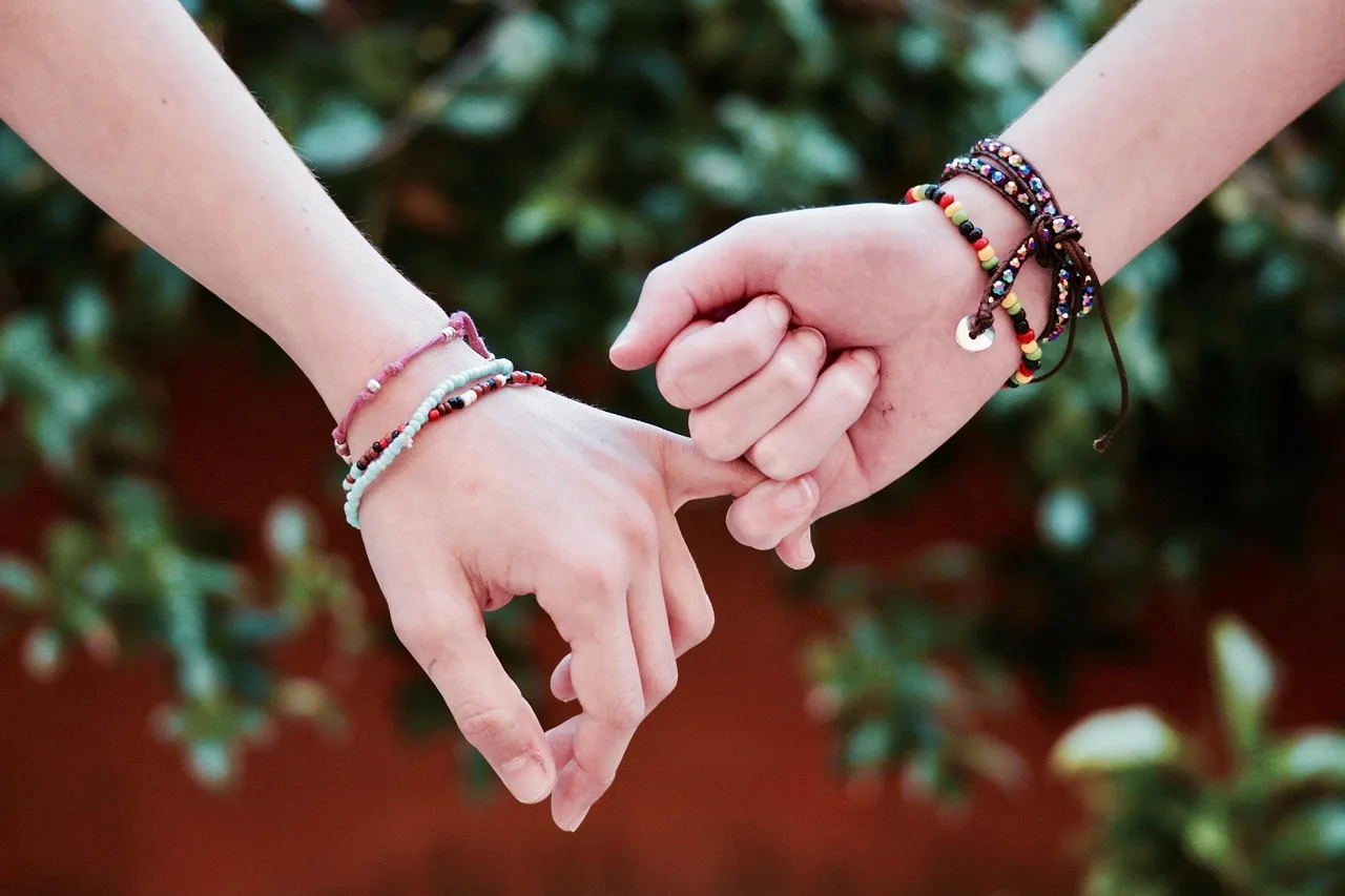 A woven thread bracelet knotted around a wrist as another hand withdraws