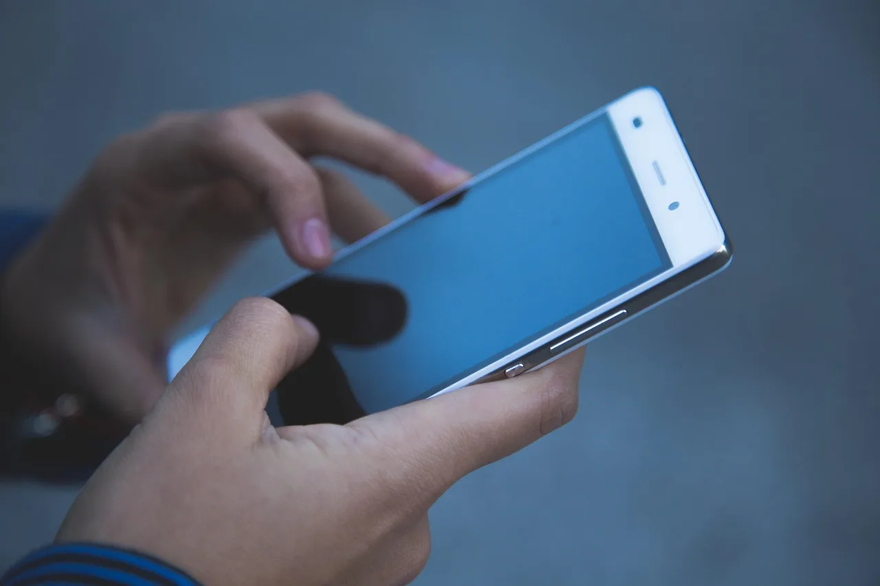 A hand holding a printed bill on a table next to a phone with its keypad open