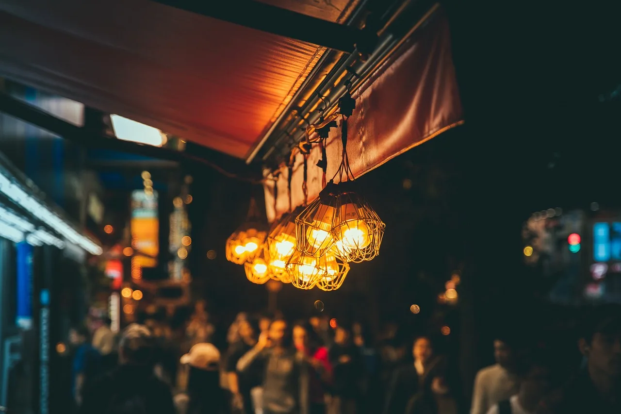 Drinkers at red plastic tables filling a narrow Seoul street at night under strings of small flags