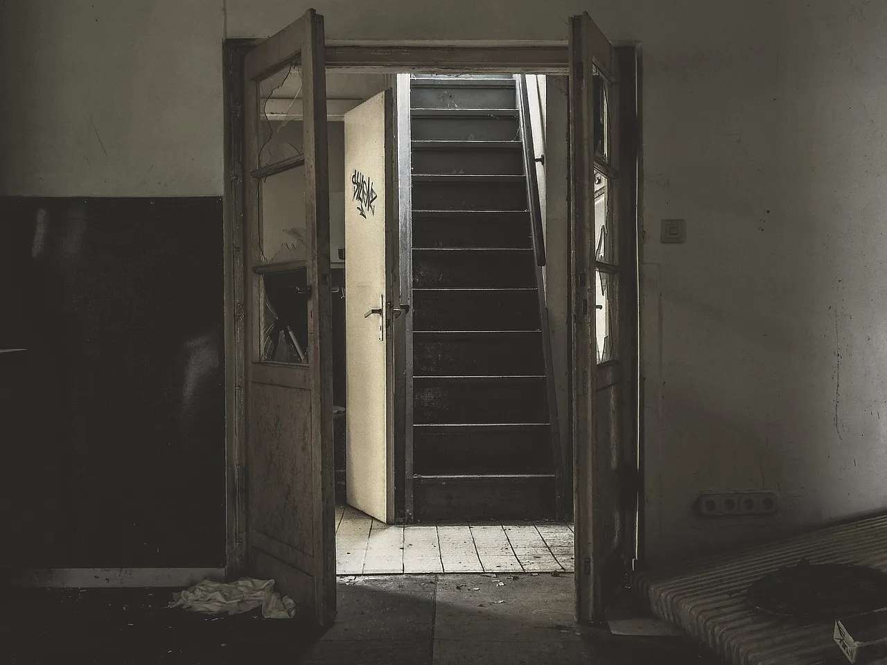 A dim concrete stairwell with a handwritten sign beside a lit metal door