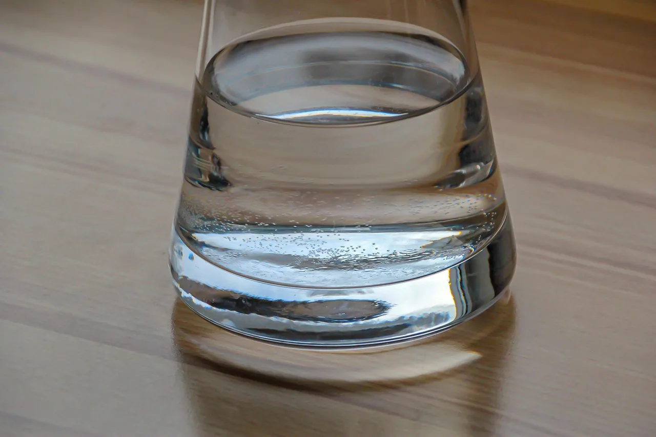 A plain glass carafe of tap water and two empty tumblers on a bistro table